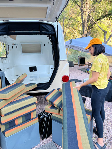 Preparing an RV rental! Woman loads striped cushions into the small travel trailer's open hatch for a comfy trip.