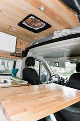 Cozy RV rental interior with wood ceiling, kitchen sink, and a large wooden table. Driver's cabin visible.