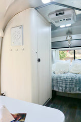 Cozy rv rental interior with light wood walls and ceiling, a bed with a cozy blanket, and a white memo board.
