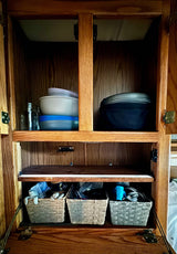 Inside an RV rental cabinet: organized dishes, jars, and practical storage baskets.