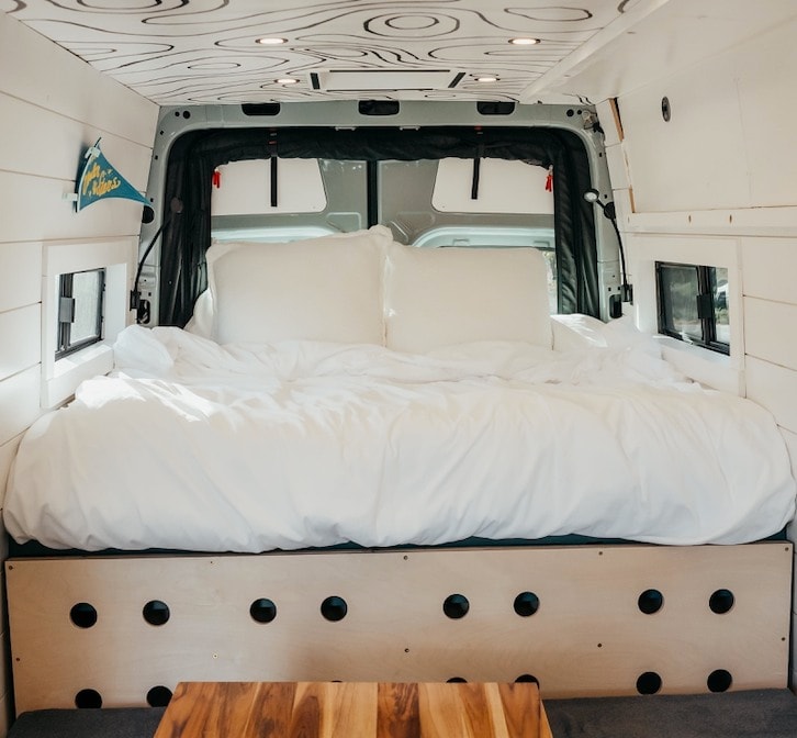  with a grey camper van set against majestic snow-capped peaks.|Comfortable RV rental interior: a large bed with white bedding — photo 2