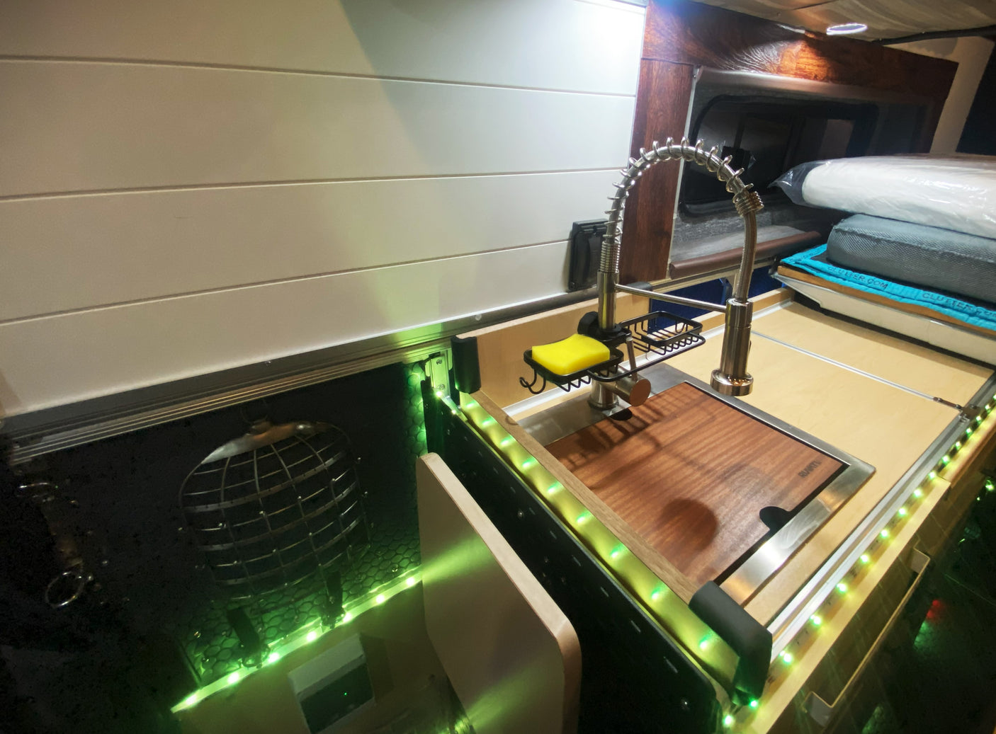This RV rental's campervan interior offers a compact kitchen with a sink, cutting board, and stylish green LED accent lighting.