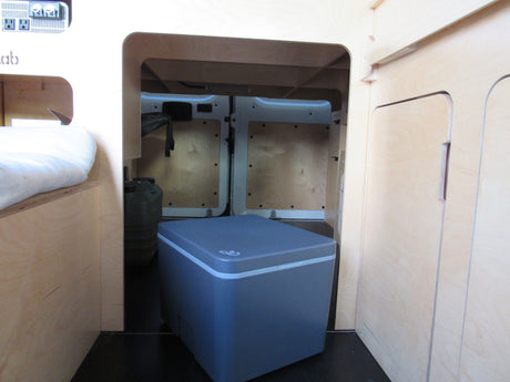 RV rental: Camper van's rear storage features a portable fridge, water jugs, and light wood interior under the bed.