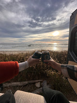 Toasting a golden beach sunset from a cozy **RV rental**. Hands clinking insulated cups for a perfect van life adventure.