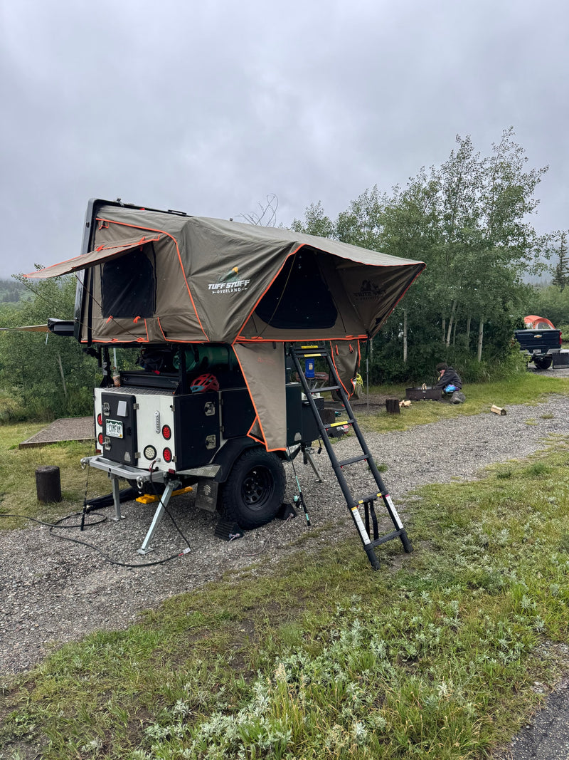 Experience overland camping with this RV rental! A gray trailer with olive rooftop tent and ladder, set up at a gravel site. — photo 9