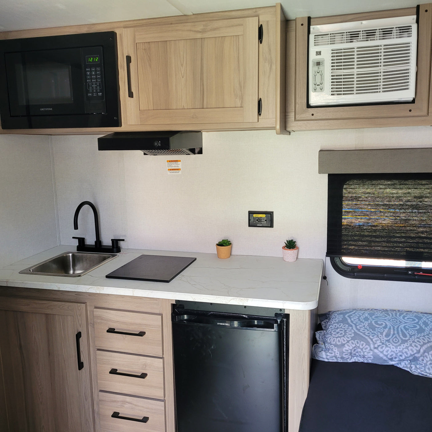 RV rental's compact kitchen. Includes microwave, sink, induction cooktop, mini-fridge, and AC unit, offering home comforts on the road.