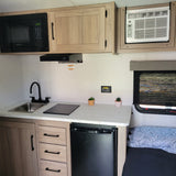 RV rental's compact kitchen. Includes microwave, sink, induction cooktop, mini-fridge, and AC unit, offering home comforts on the road.