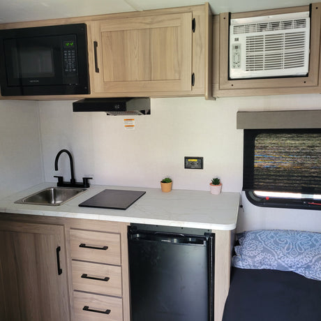 RV rental's compact kitchen. Includes microwave, sink, induction cooktop, mini-fridge, and AC unit, offering home comforts on the road.