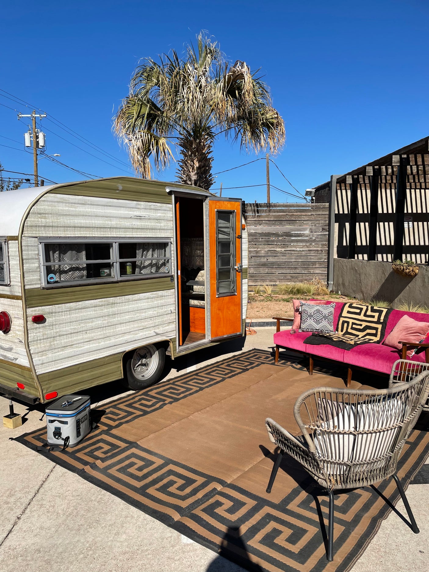 Experience unique outdoor living! This cozy vintage **rv rental** features a vibrant pink couch, rug, and palm trees under a clear sky.