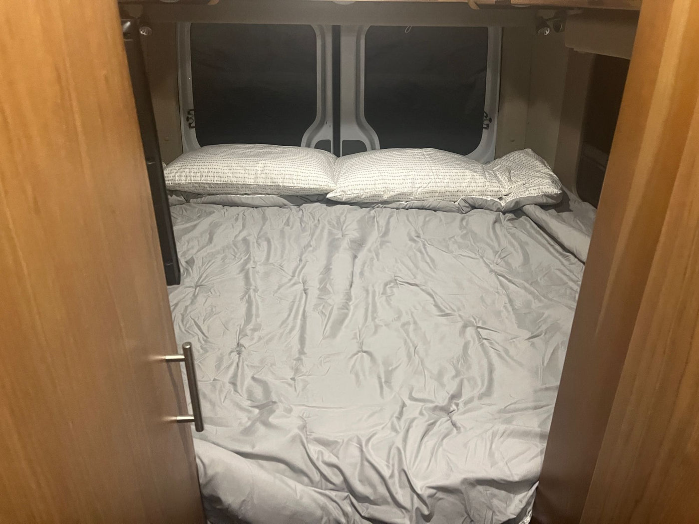 Cozy RV rental sleeping area with a made bed, gray sheets, and pillows in a camper van. — photo 12
