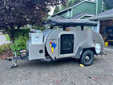 This compact rv rental is a silver teardrop camping trailer, equipped with an awning and storage for travel adventures.
