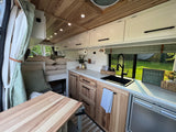 Stylish rv rental camper van interior: bright kitchen, natural wood cabinetry, and a cozy bed area.
