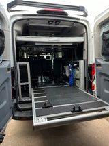 RV rental: Rear of a custom camper van conversion showing a bed platform, extended slide-out tray, and water system.