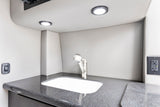 RV rental bathroom/kitchenette: compact sink, modern faucet, dark counter, and bright LED lights. Features switches & outlet.