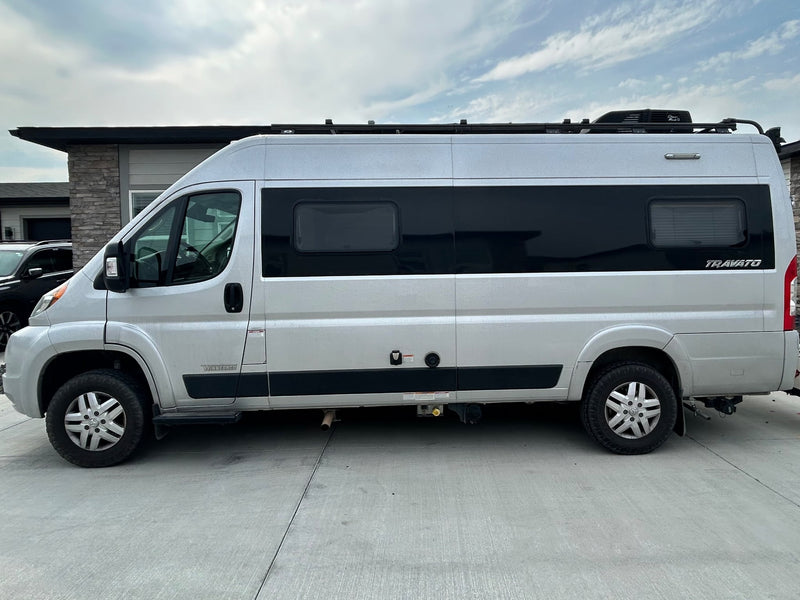 Silver Winnebago Travato rv rental parked on concrete. Side view shows tinted windows and a roof rack.|A silver Winnebago Travato camper van — photo 1