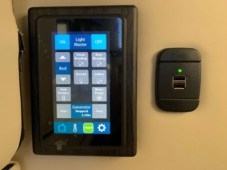 An RV rental's digital control panel and USB charging station. The touchscreen manages lights, water pump, and generator functions.