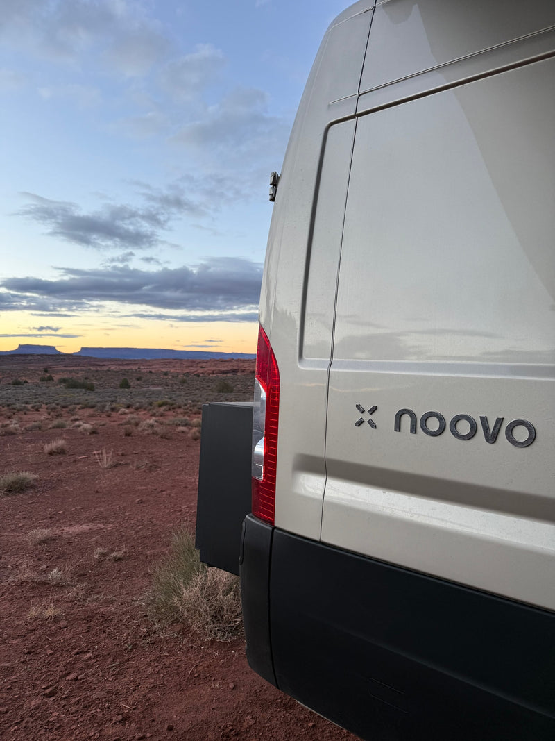 An rv rental van with a 'noovo' logo, parked in a vast desert landscape at dusk, with mesas under a cloudy sky. — photo 8