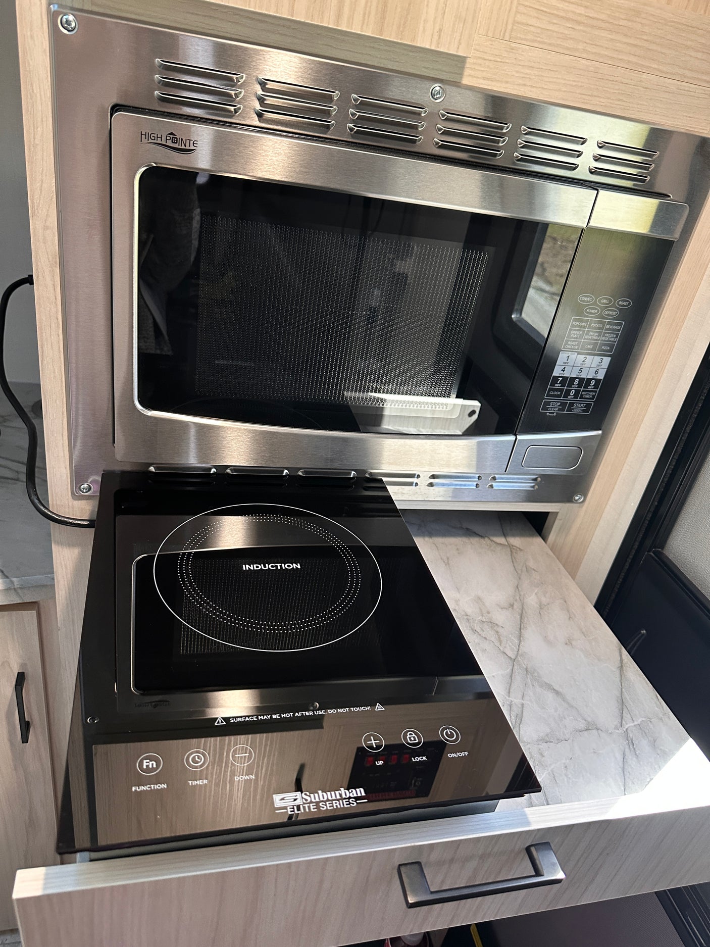 Compact RV rental kitchen with a High Pointe microwave oven and a Suburban Elite Series induction cooktop for efficient cooking.