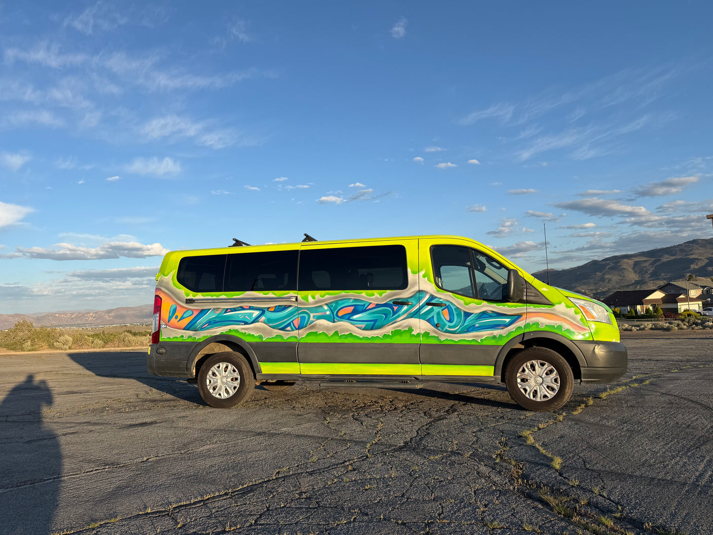 A bright yellow RV rental van, customized with graffiti artwork, is parked on cracked pavement with mountains in the background.