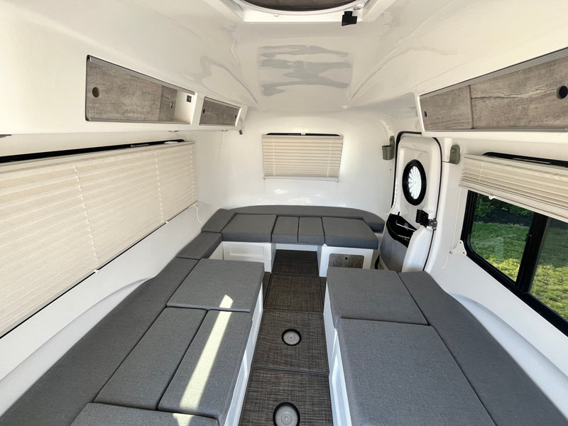 Clean RV rental interior: U-shaped grey seating converts to beds, with overhead storage, blinds, and dark floor for travel. — photo 14