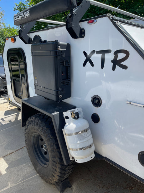 White off-road RV rental camper with "XTR" decal, a robust storage case, propane tank, and a "KICKASS" awning.