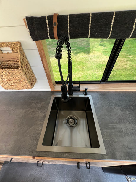 Compact RV rental kitchen features a sleek black faucet, stainless sink, and dark countertop for easy living on the go.
