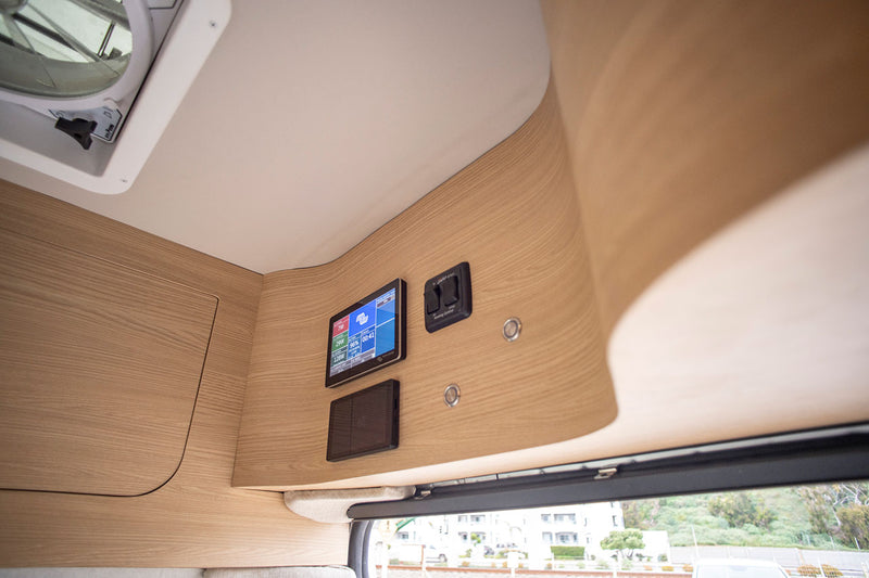 RV rental interior: light wood paneling, digital power display, awning controls, and a ceiling vent. — photo 20