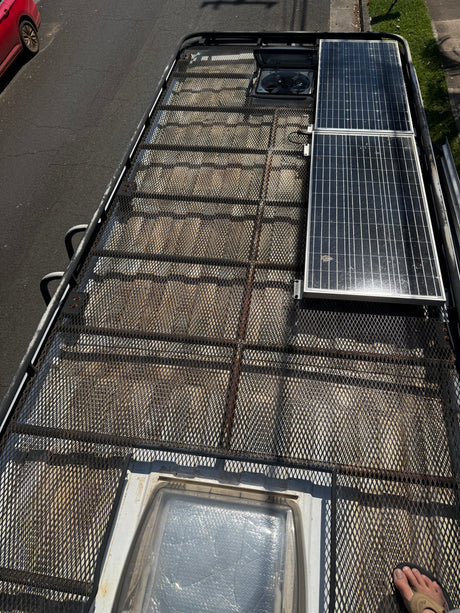 Top-down view of an RV rental van's roof rack with solar panels, fan, and skylight.
