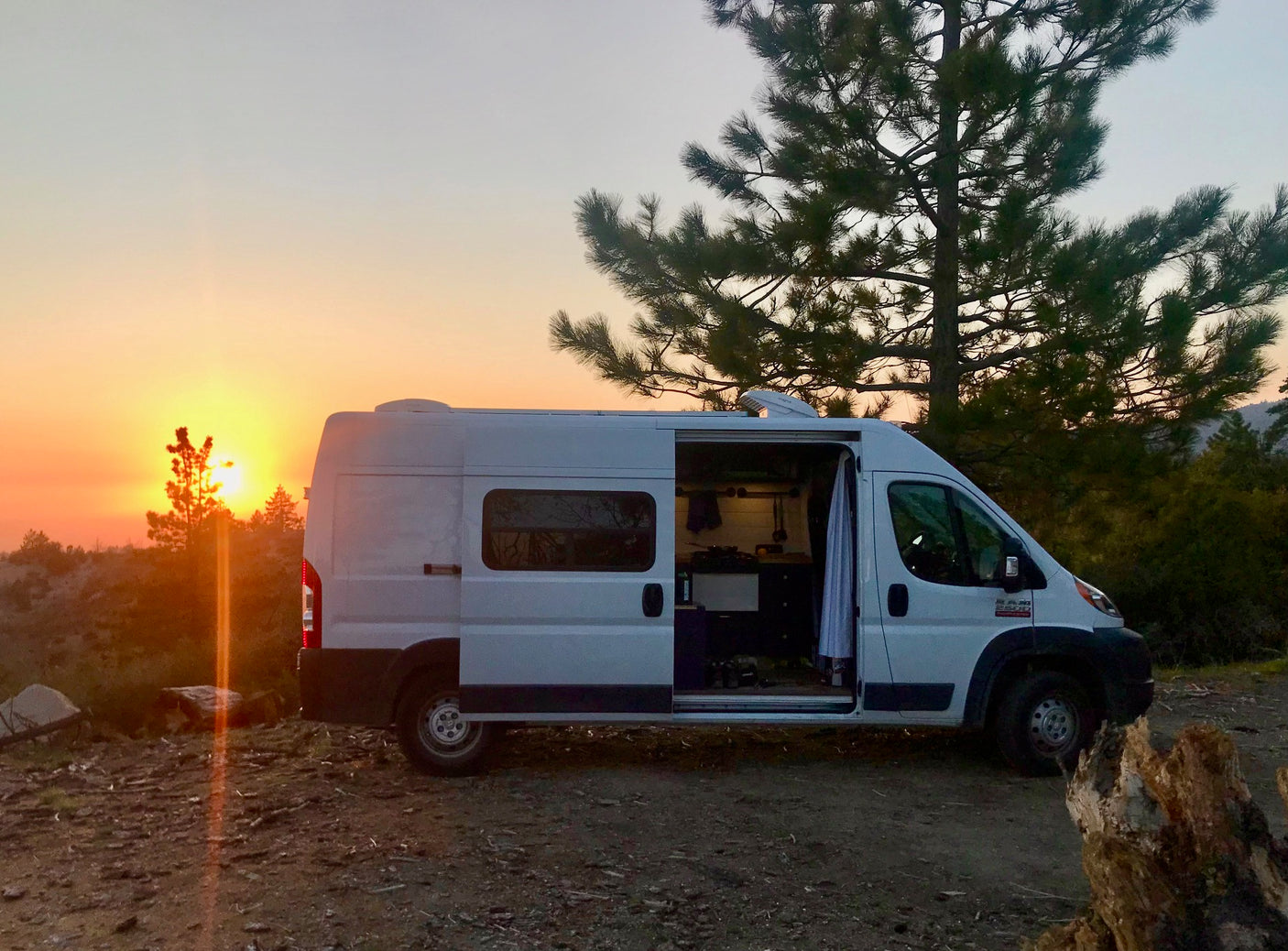 Experience van life with an rv rental! White camper van at sunset, door open to interior, surrounded by nature.