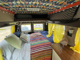 Cozy camper van interior for rv rental, featuring a comfortable bed, vibrant blankets, and unique ceiling art.