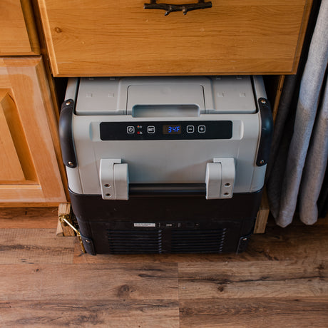 Compact portable refrigerator in an rv rental, displaying 34F, securely placed under wooden cabinets for travel convenience.