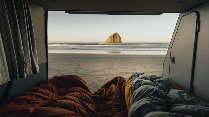 Inside an RV rental, two sleeping bags face a serene beach with a large sea stack in the ocean. — photo 5