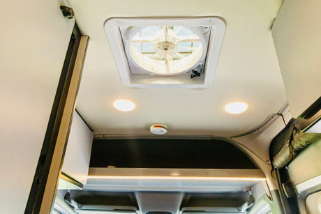 RV rental interior showing a ceiling fan, two bright lights, a smoke detector, and overhead storage.