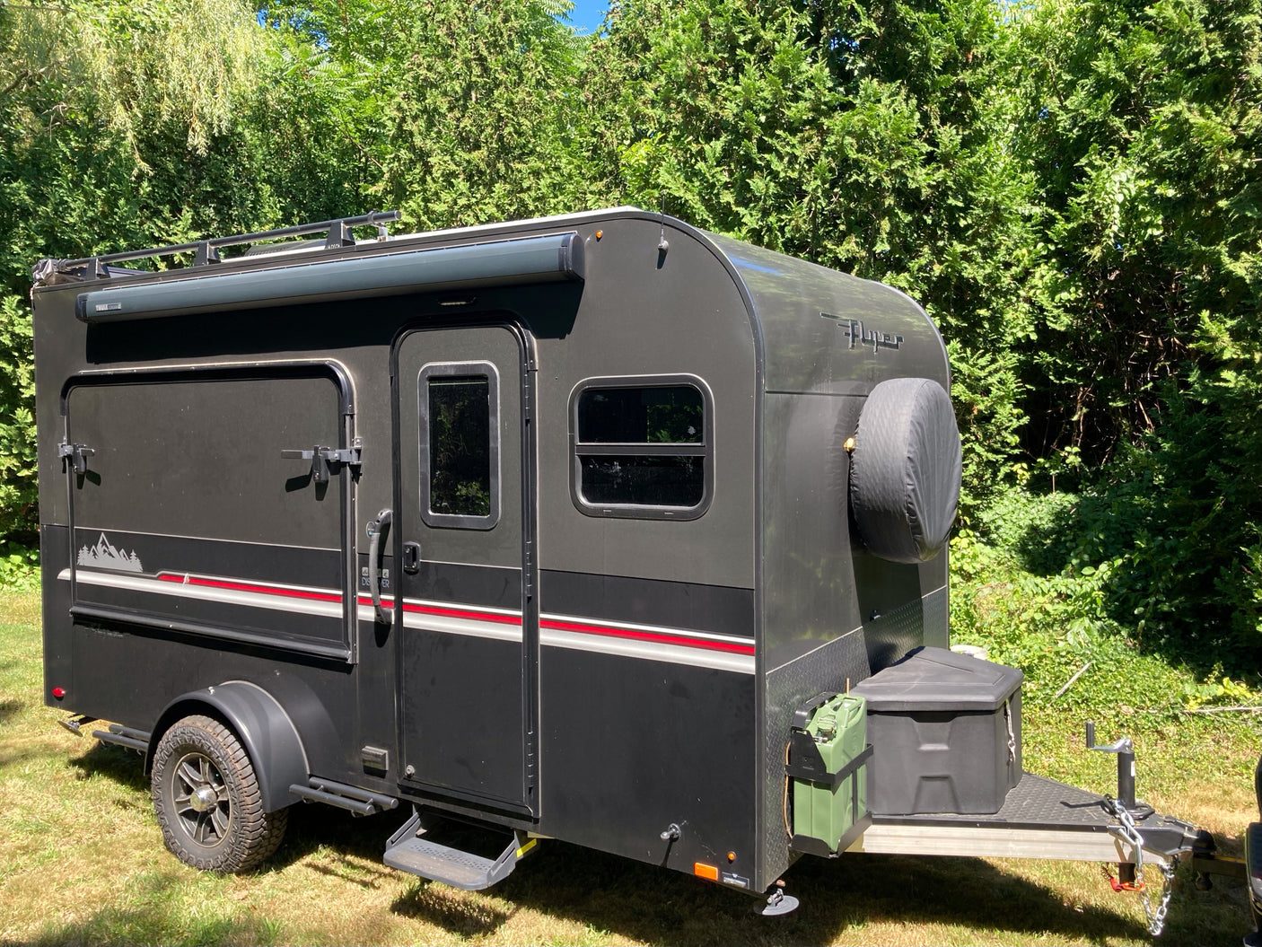 A sleek black teardrop camping trailer, ideal for an RV rental adventure, features off-road tires, roof rack, and side awning.