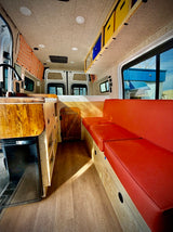 Step inside this modern RV rental! Features a compact kitchen, comfy red bench seating, and rear bed for mobile living.