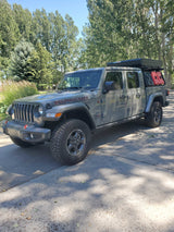 Gray Jeep Gladiator Rubicon with rooftop tent & fuel cans. An overland rig perfect for adventures, or a rugged rv rental option.