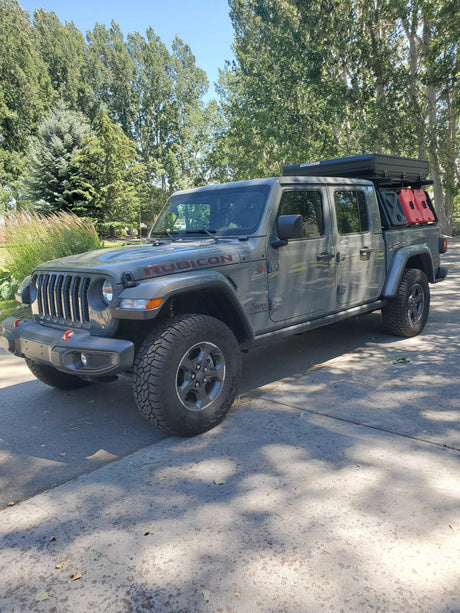 Gray Jeep Gladiator Rubicon with rooftop tent & fuel cans. An overland rig perfect for adventures, or a rugged rv rental option.