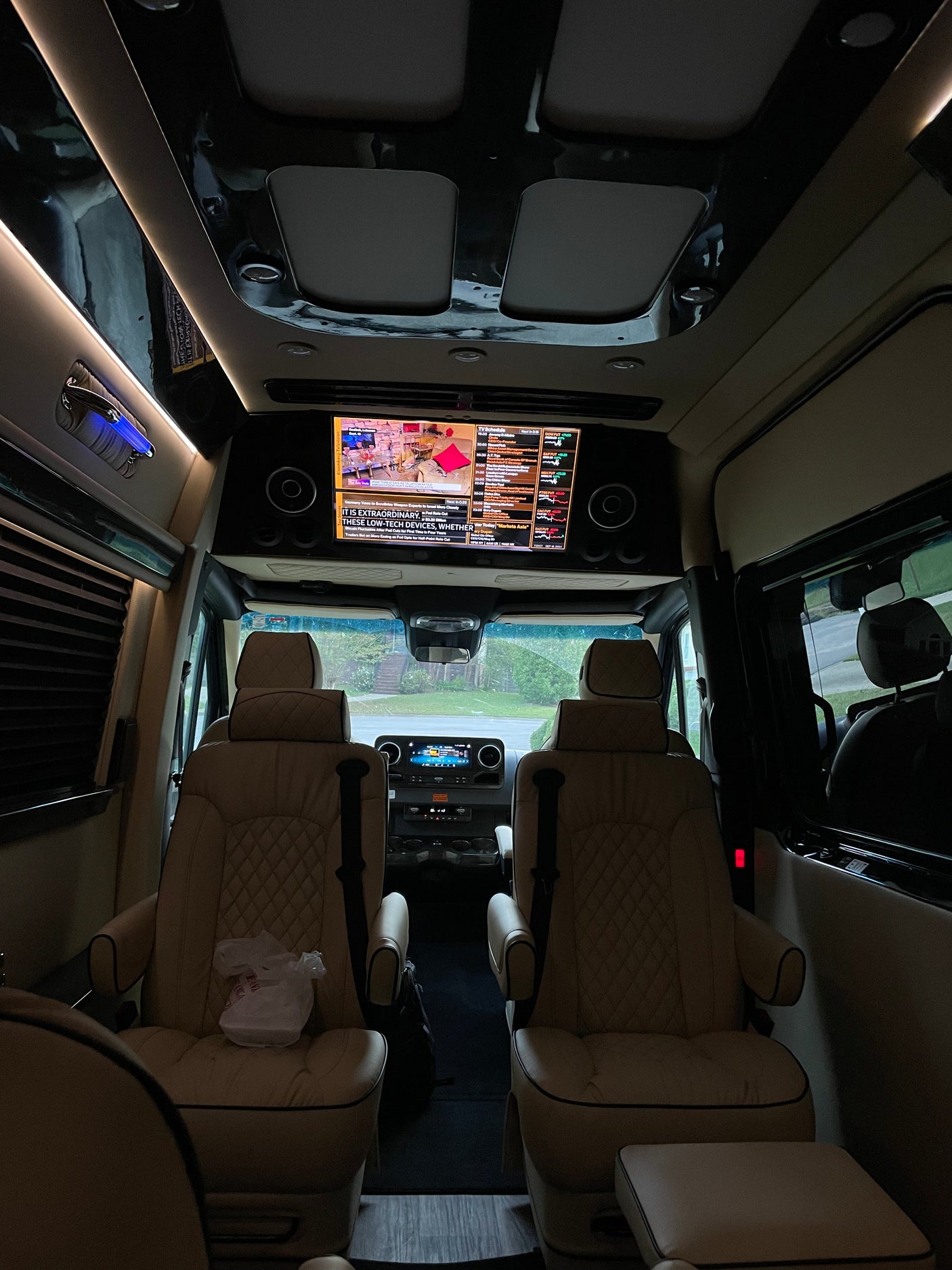 Luxurious RV rental interior features plush captain's chairs, reflective ceiling, and a large screen displaying Bloomberg TV.