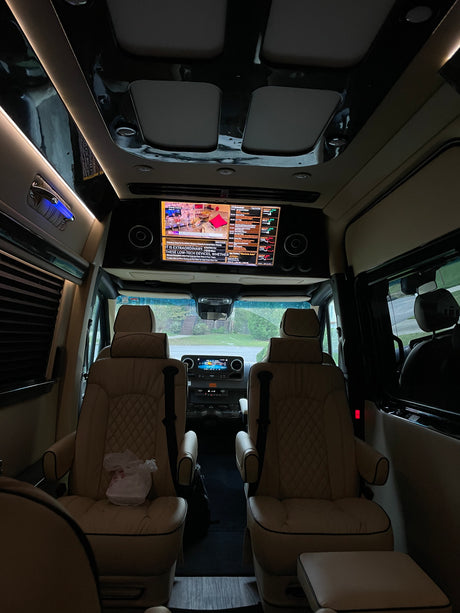 Luxurious RV rental interior features plush captain's chairs, reflective ceiling, and a large screen displaying Bloomberg TV.