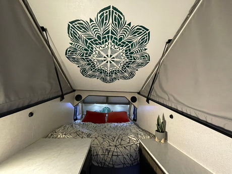 Cozy A-frame RV rental bedroom with a decorative mandala ceiling, comfy bed, and side storage.