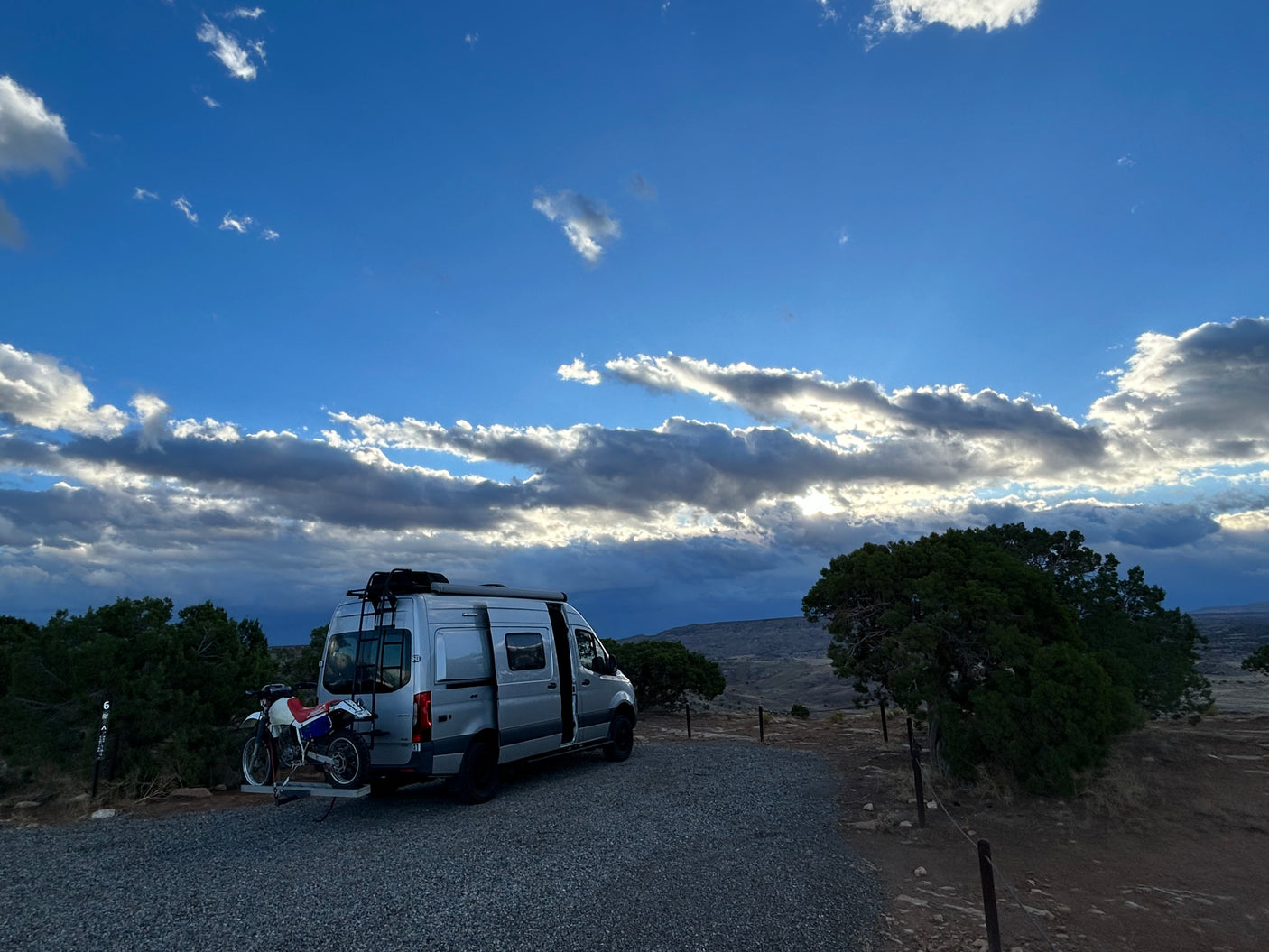 Scenic RV rental camper van with dirt bike at a tranquil campsite under a dramatic sky, perfect for outdoor adventure.
