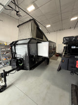Sleek black overland camper with pop-up tent, side open, parked in a warehouse. Ideal for your next rv rental adventure.