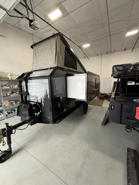 Sleek black overland camper with pop-up tent, side open, parked in a warehouse. Ideal for your next rv rental adventure.