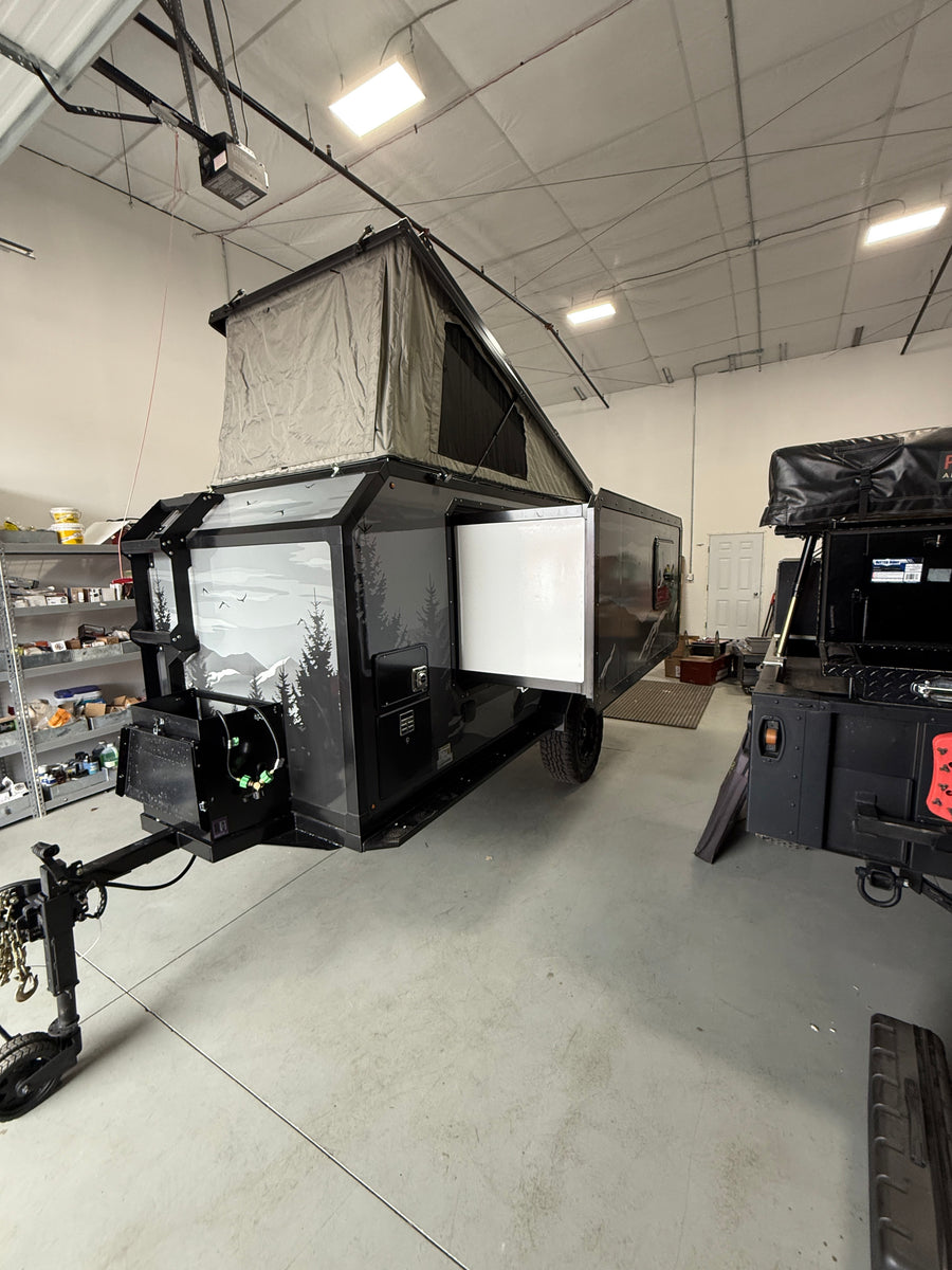 Sleek black overland camper with pop-up tent, side open, parked in a warehouse. Ideal for your next rv rental adventure.