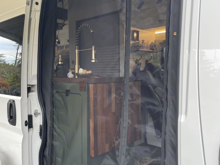  and a folding extension.|Cozy RV rental interior with bed and windows showing the outside. Perfect for van life adventures.|RV rental interior with modern subway tile backsplash — photo 7
