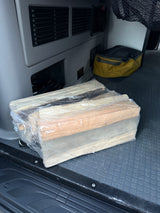 A plastic-wrapped bundle of firewood sits on the black floor of an RV rental, ready for a camping trip.