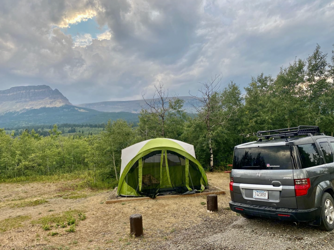 A green tent and grey car parked at a beautiful mountain campsite. Enjoy the outdoors—whether with an RV rental or a tent.