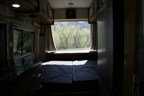 Step inside this RV rental: a comfy bed, kitchen area, and a large rear window offering stunning views of green trees and mountains.