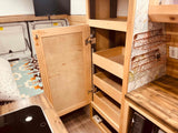 RV rental's light wood interior features an open cabinet with pull-out storage, a compact kitchen, and wall decor.