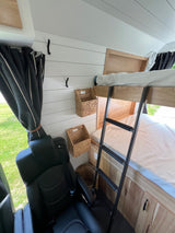 Modern RV rental interior with bunk beds, a ladder, woven storage baskets, and comfortable black leather seating.